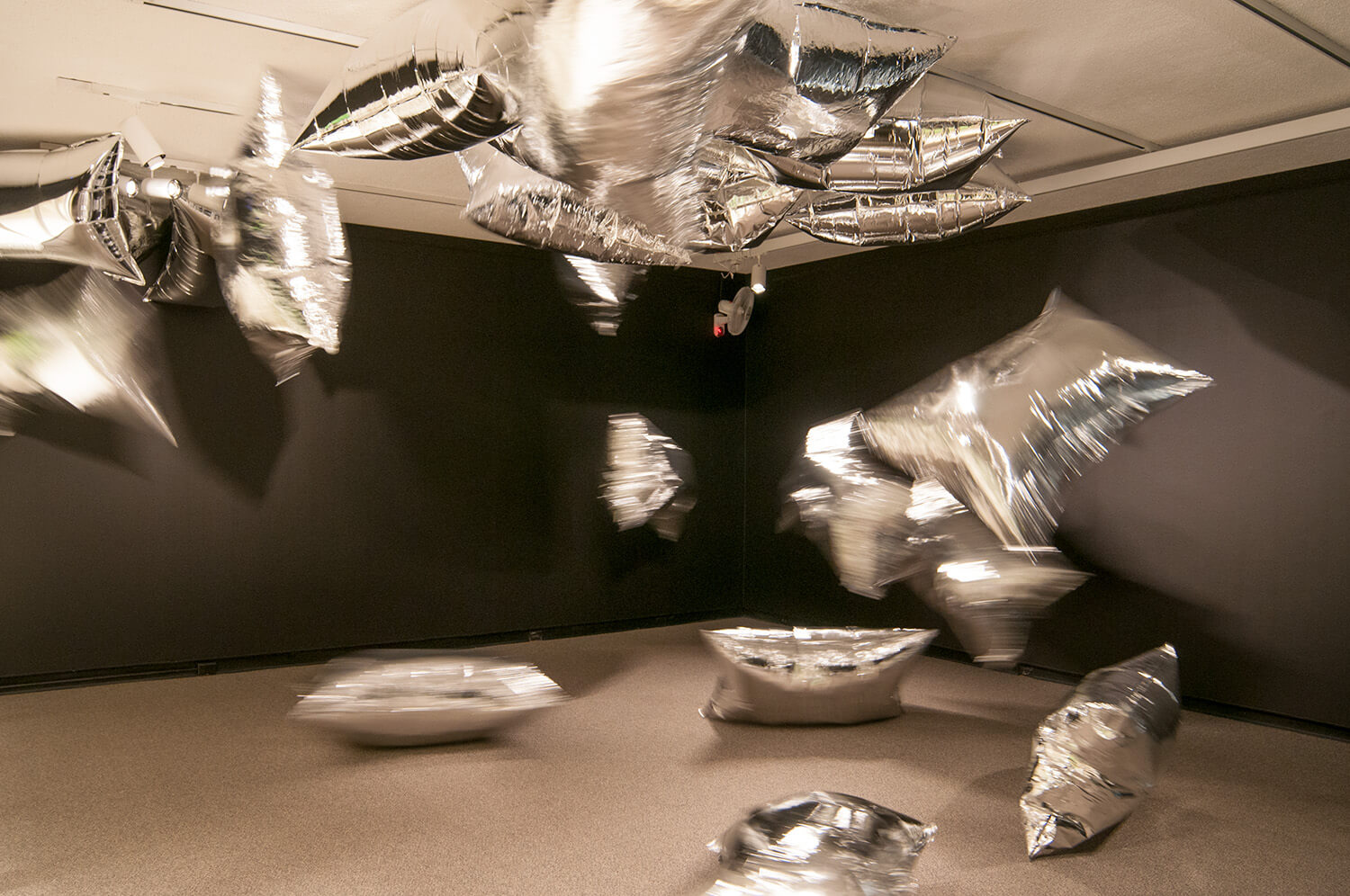 Shiny silver balloons fly through the air in a small, enclosed room.