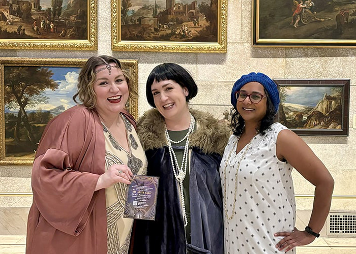 Three women in 1920s-inspired clothing smiling together in the Fountain Court.