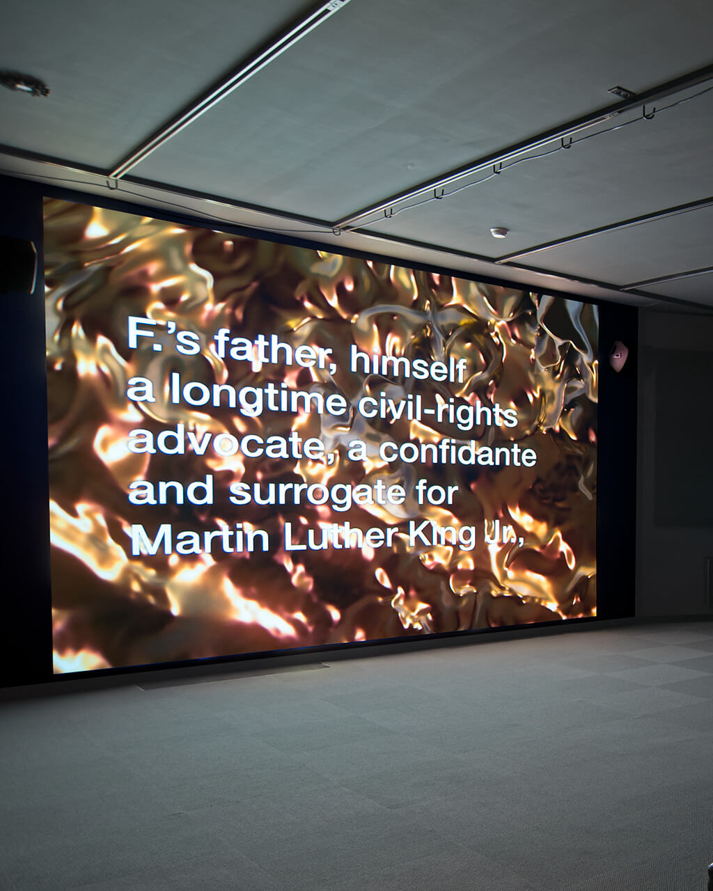 The Media Arts Watch Gallery, dark, with Tony Cokes's "The Queen is Dead...Fragment 2" playing on one wall.
