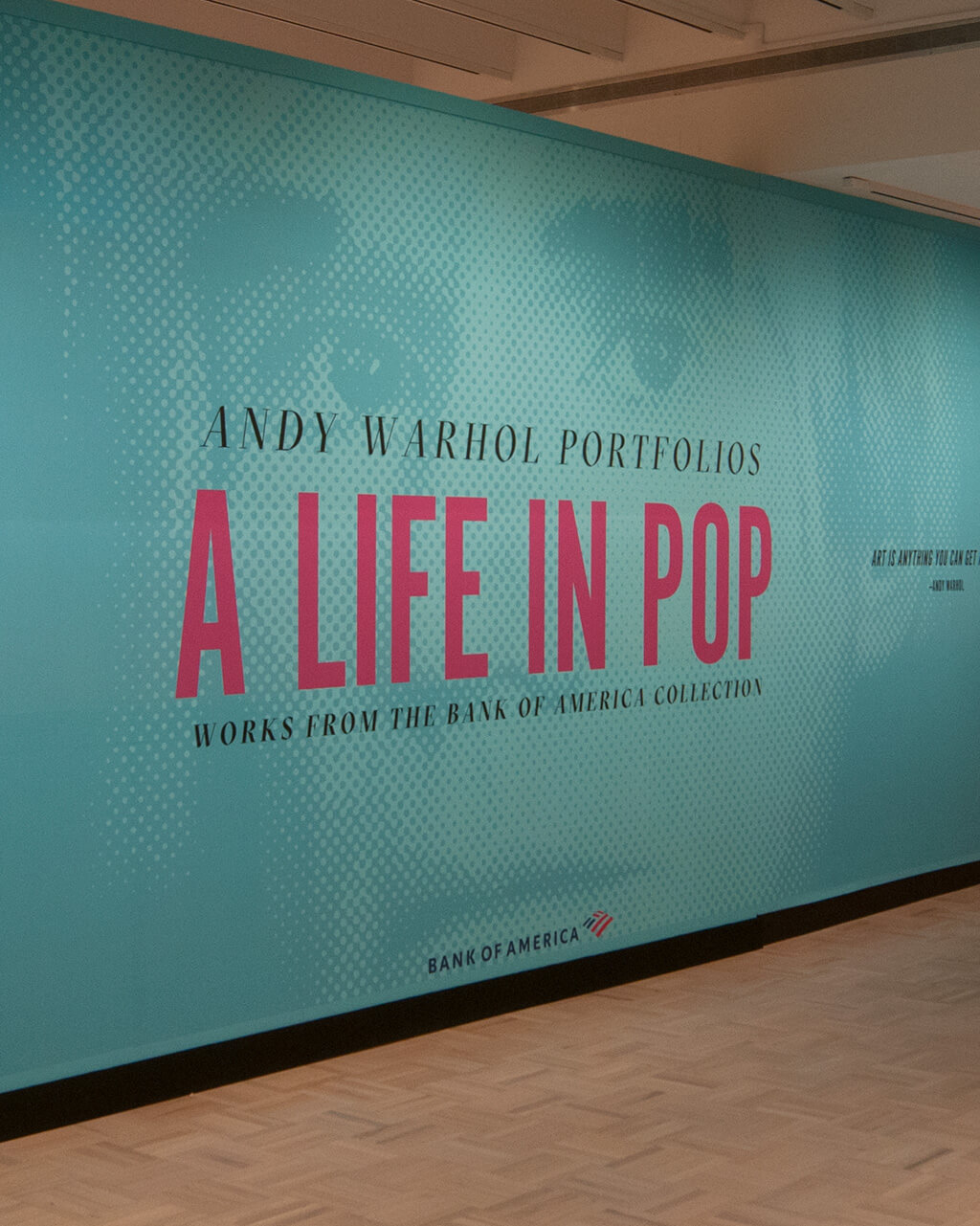 The title wall of the exhibition "Andy Warhol Portfolios: A Life in Pop," with some prints on a wall in the background.