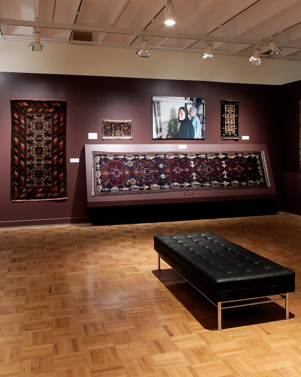 Rugs hanging on dark maroon walls in a gallery space.