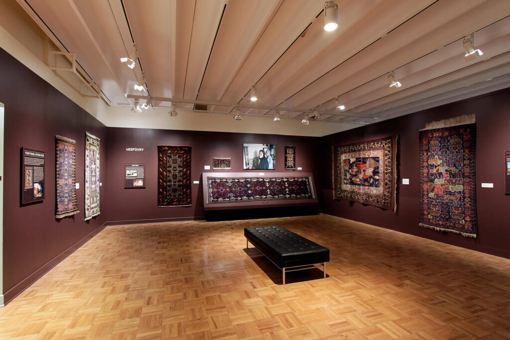 Rugs hanging on dark maroon walls in a gallery space.