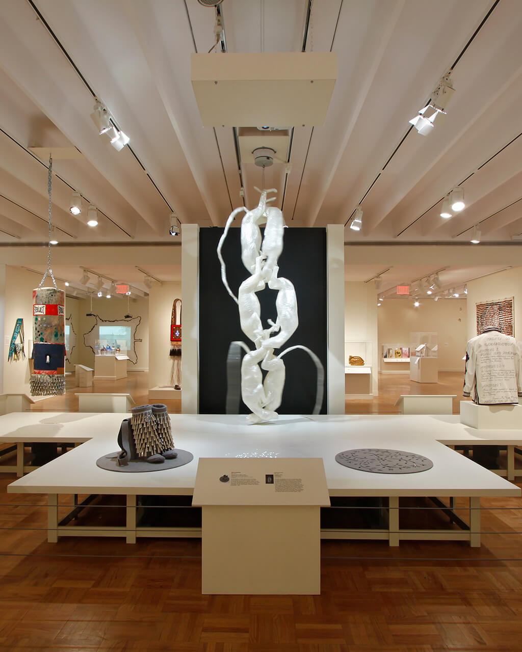 Art in many different mediums hanging on walls, the ceiling, or resting on a large platform in the middle of a white-walled gallery.