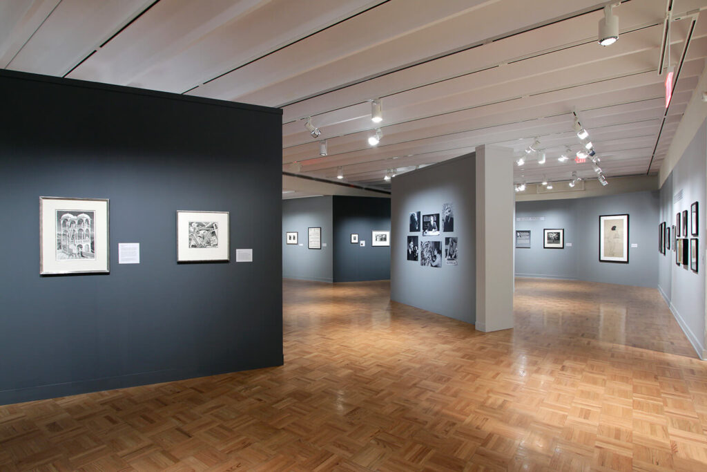 Small, framed works of art and photographs on angled walls painted dark and light gray.