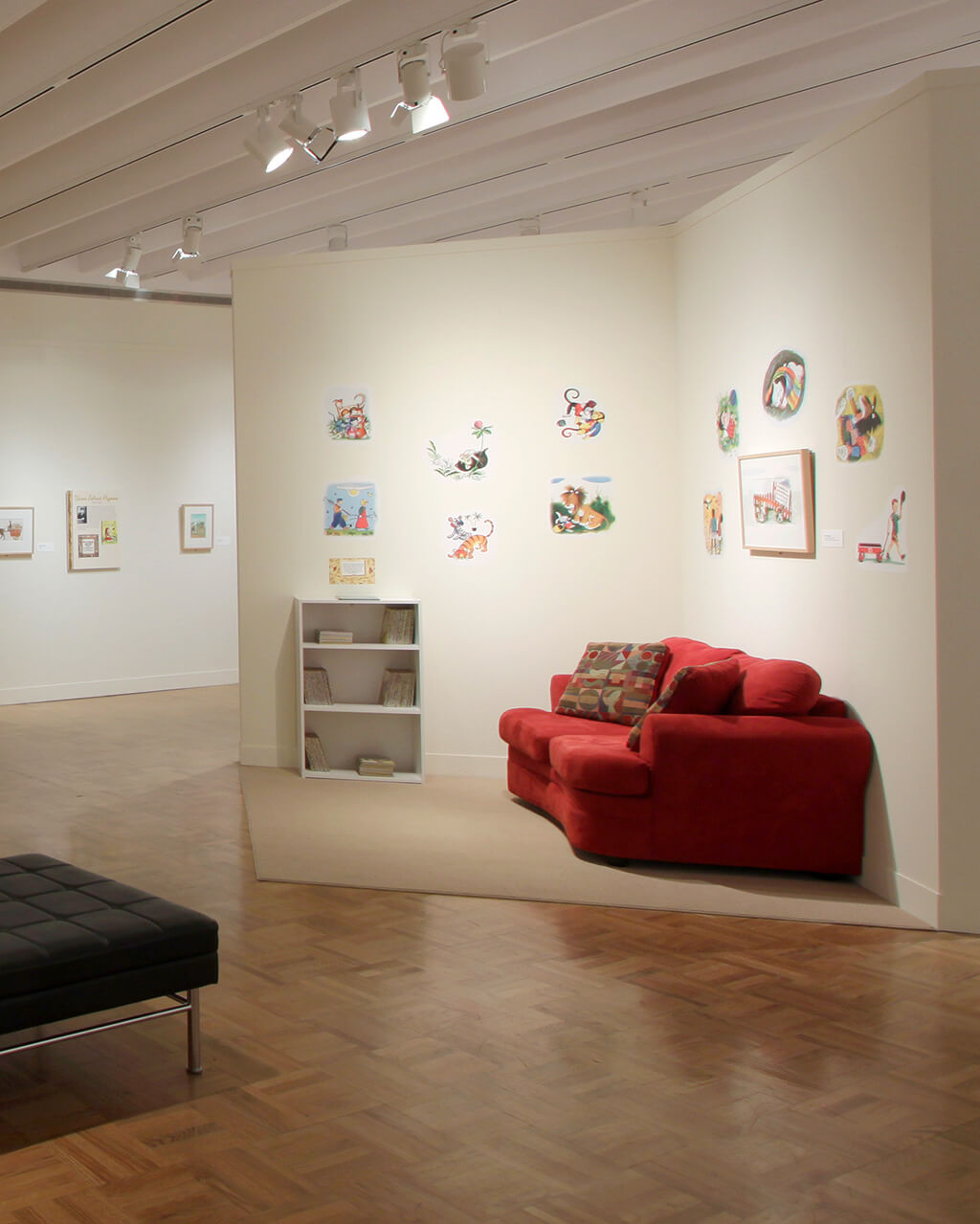 A wide gallery space with children's book illustrations on the walls and little nooks with comfy couches for sitting in three spots around the room.