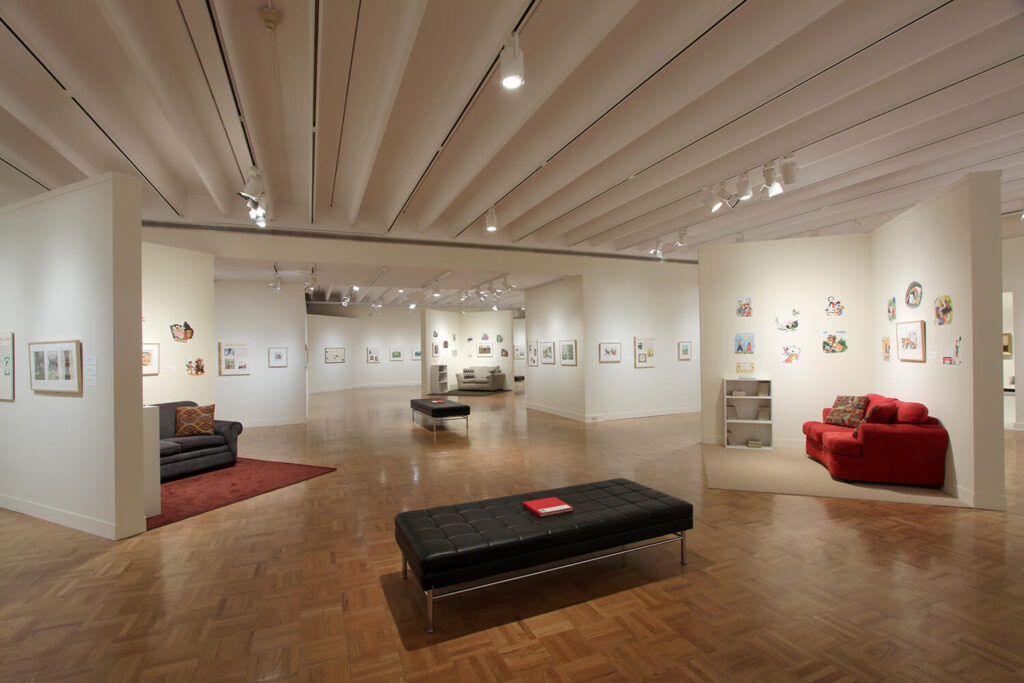 A wide gallery space with children's book illustrations on the walls and little nooks with comfy couches for sitting in three spots around the room.