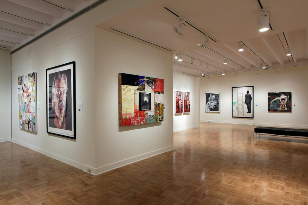 Framed works of art by many artists that all depict human beings in different ways hung on white walls in a gallery.