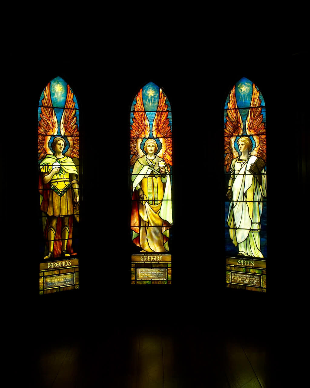 Stained glass windows depicting angels, shining in a dark room.
