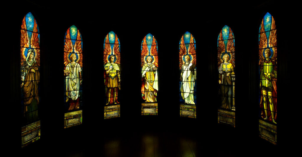 Seven stained glass windows depicting angels, shining in a dark room.