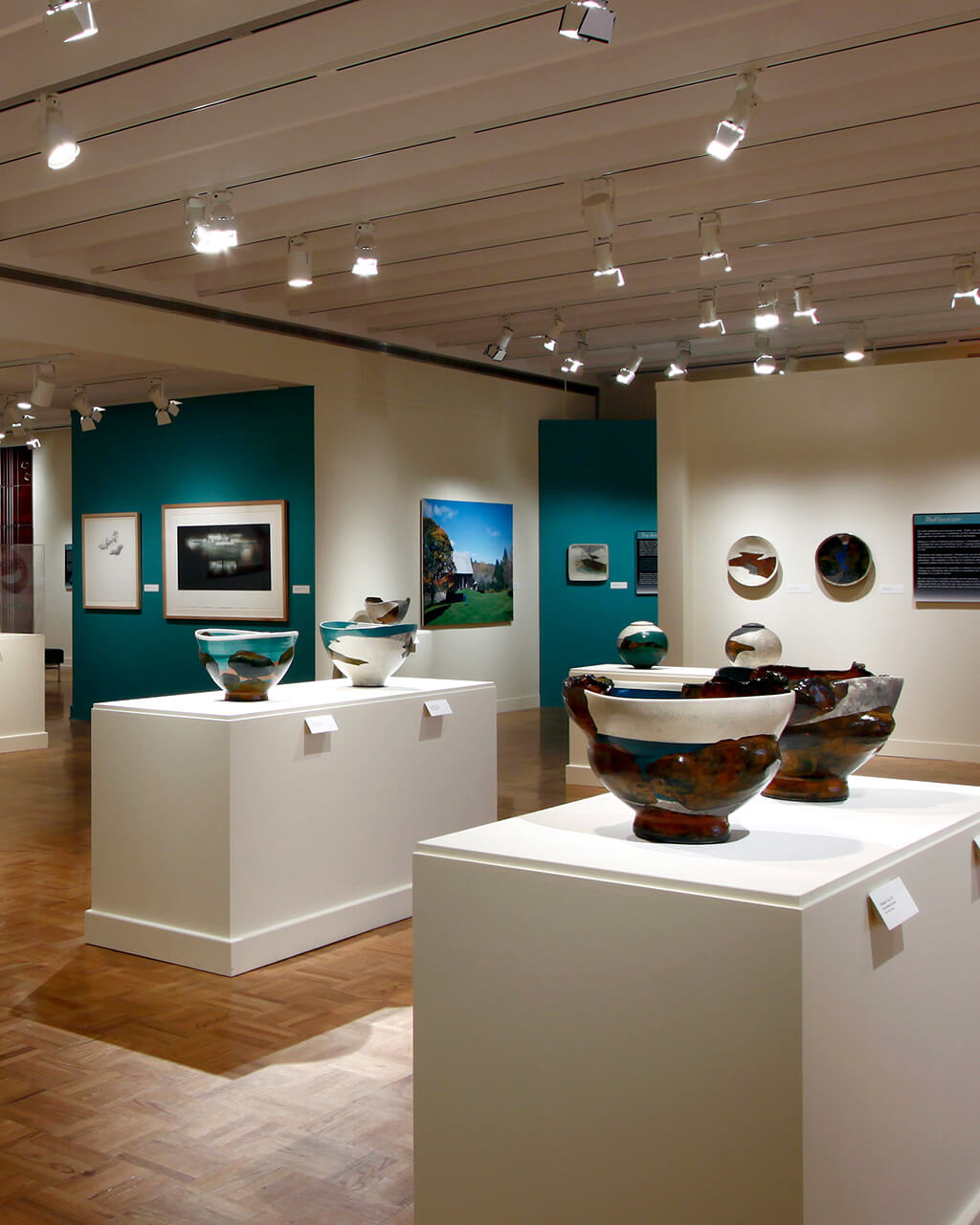 Ceramic vessels on pedestals in a wide gallery space, with other works of art by Wayne Higby hanging on the walls.