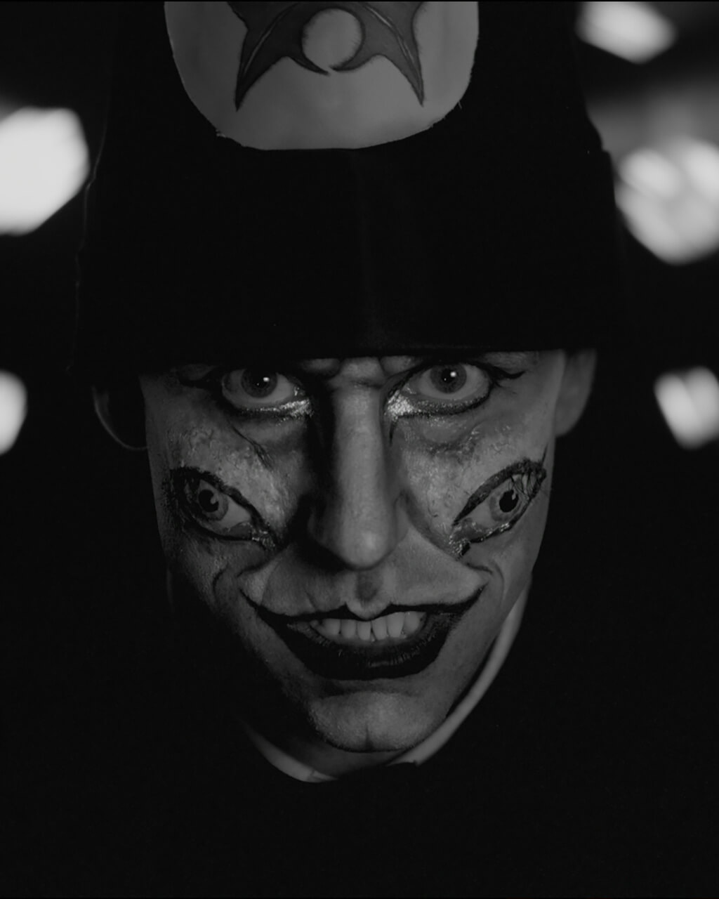 A man with eyes painted on his cheeks stares down the camera unsettlingly.