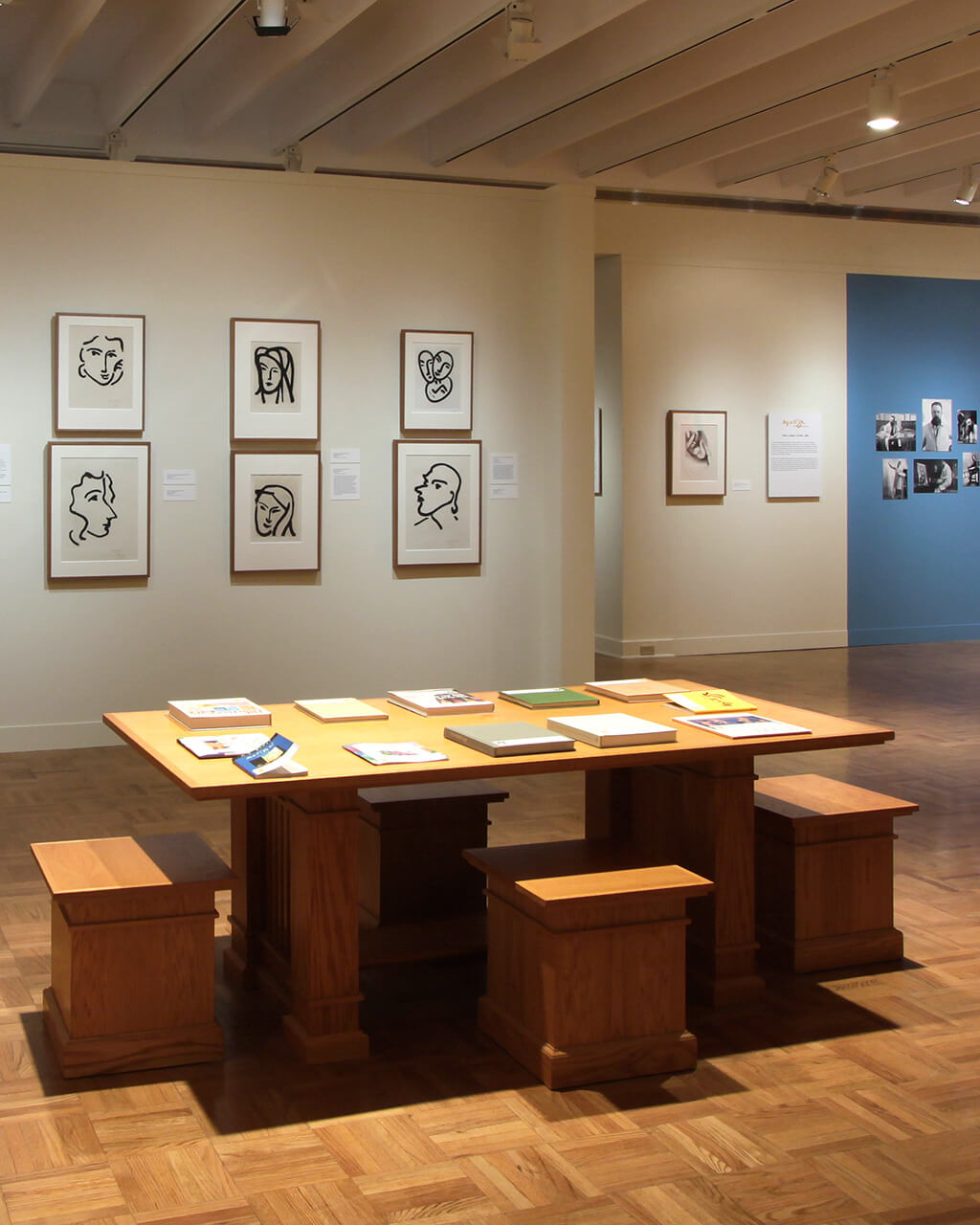 Framed prints by Henri Matisse on walls in a large gallery space. In the foreground is a wooden table with activities on it.