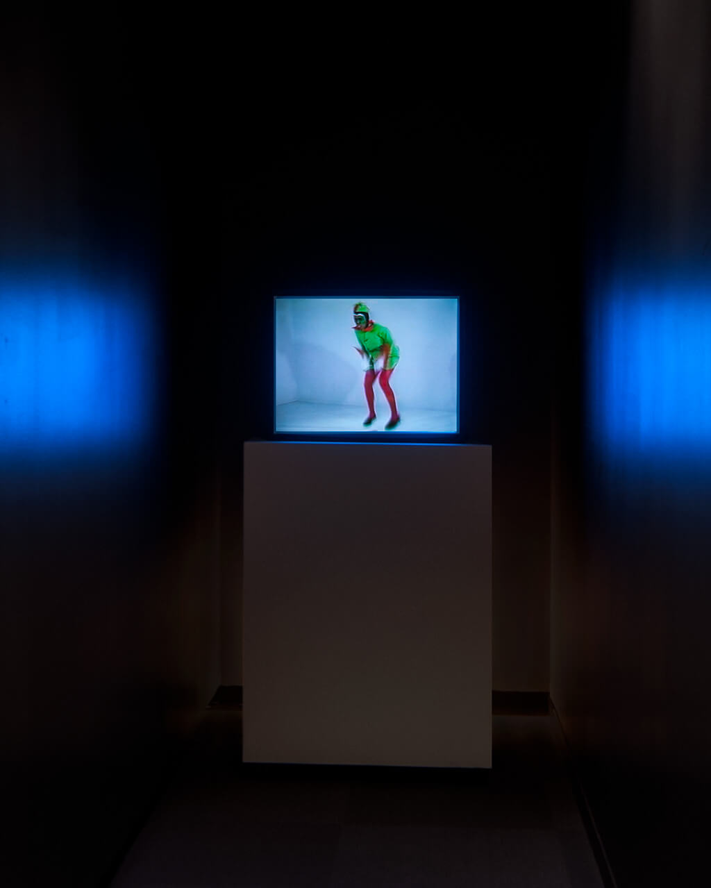 A man in a green jester's costume jumps up and down on a small TV screen in a small, very dark room.