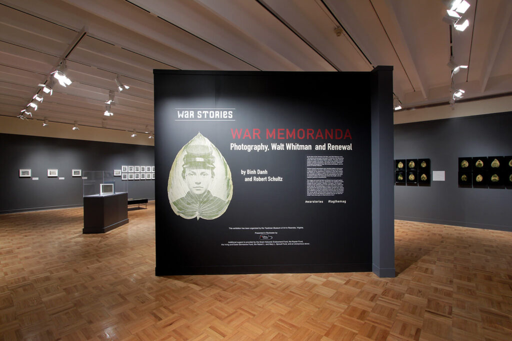 The title wall of the "War Memoranda" exhibition, with text and artwork on a charcoal gray painted wall.