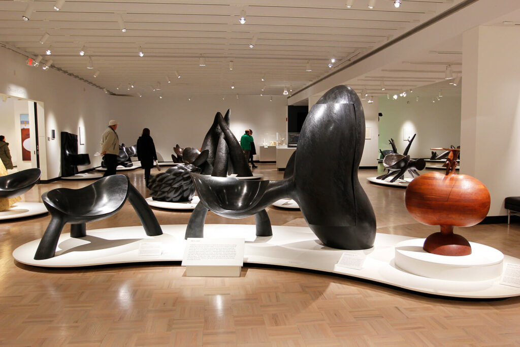 Organically-shaped wooden furniture sculptures by Wendell Castle on view in a large, white-walled gallery.