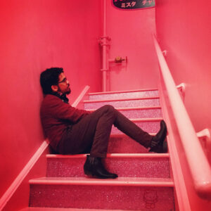 Gabriel Cruz sitting in a neon pink stairwell.