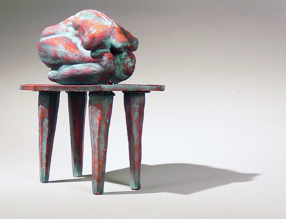 A ceramic sculpture of an organic shape on top of a table, painted like rusting iron