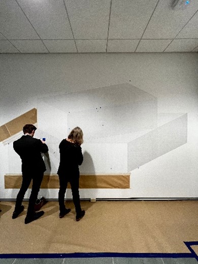 Two people in the process of drawing Sol LeWitt's Form Derived from a Cube on the wall of the Vanden Brul pavilion.