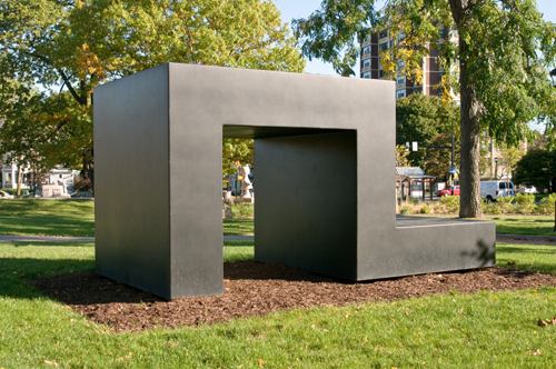 Blocky metal sculpture shaped like a hook with the opening on the ground