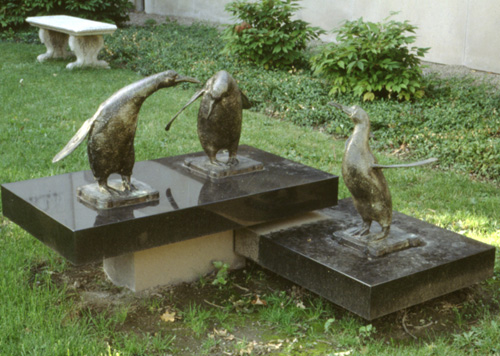 Metal statue of three penguins, flapping their wings and interacting with each other