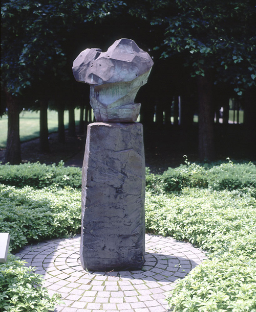 Dark clay statue of an organic form atop a tall plinth