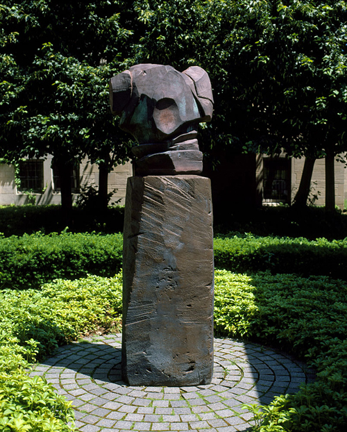 Dark clay statue of an organic form atop a tall plinth