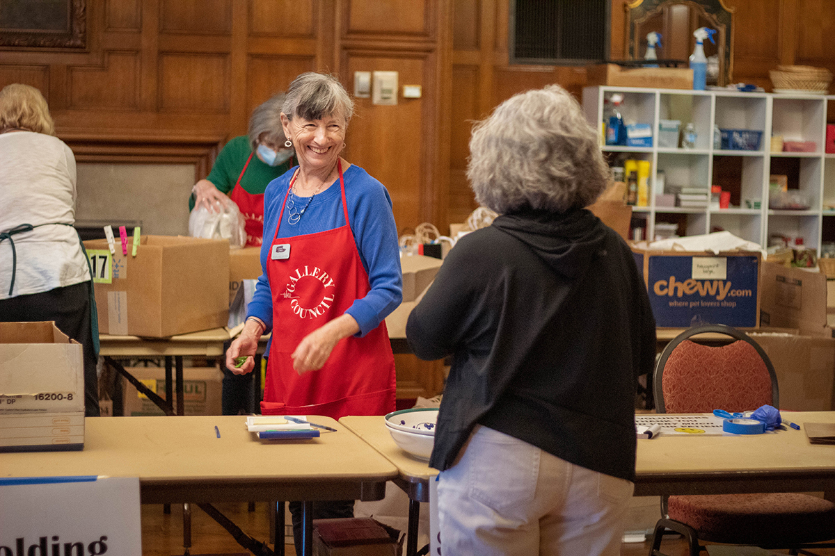 A customer checking out at Art & Treasures, a Gallery Council volunteer smiling widely at them