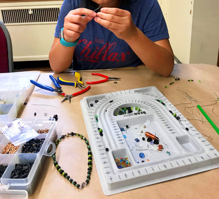 Child working on threading beads together to make a necklace