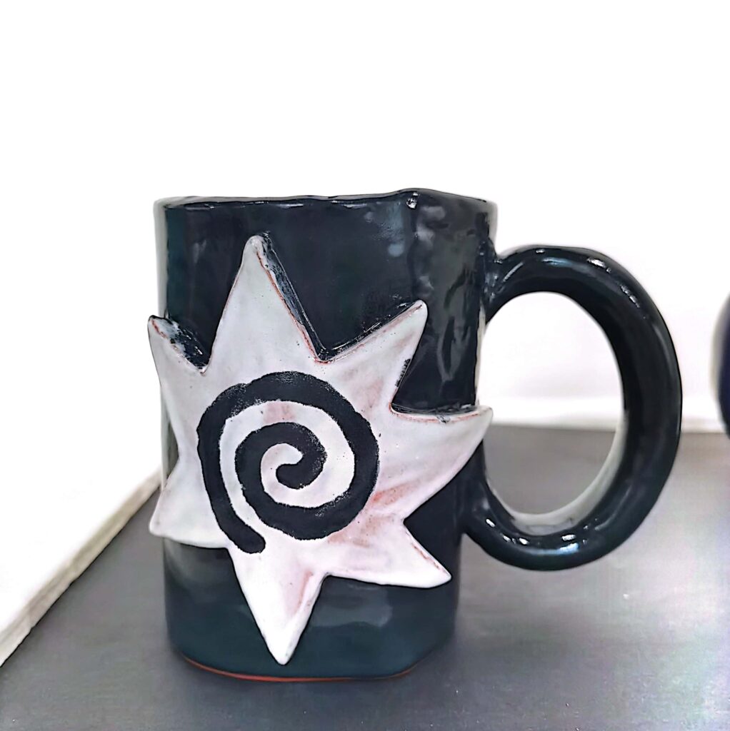 A glazed black mug with a clay star and swirl on the side