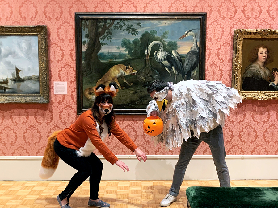 Two people dressed up as a fox and a heron in front of the painting The Fox and the Heron