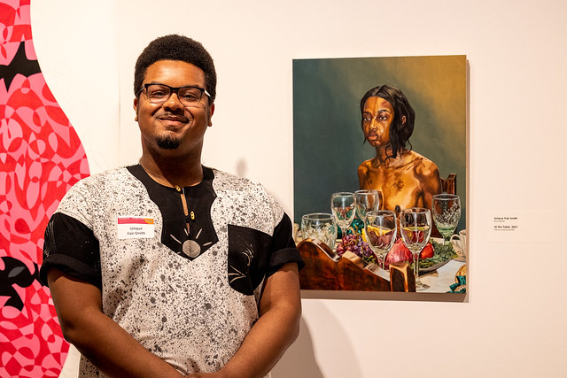 Artist Unique Fair-Smith standing next to his work of art on exhibition