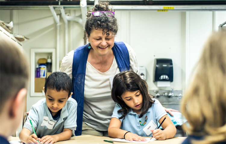 Rose Van Tyne looks over the shoulder of two young students in class