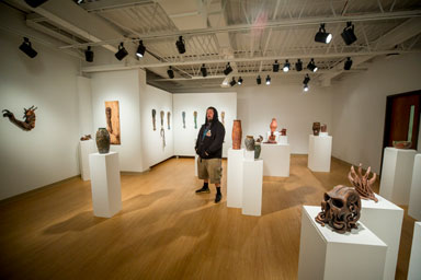 jason Ferguson standing in the middle of an exhibition of ceramic art