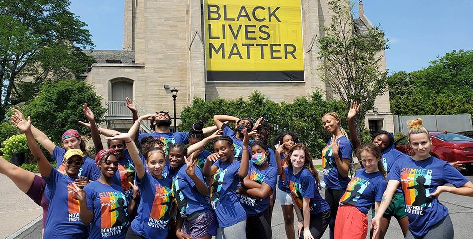 Teens standing in the Centennial Sculpture Park, the Black Lives Matter banner on Cutler Union in the background