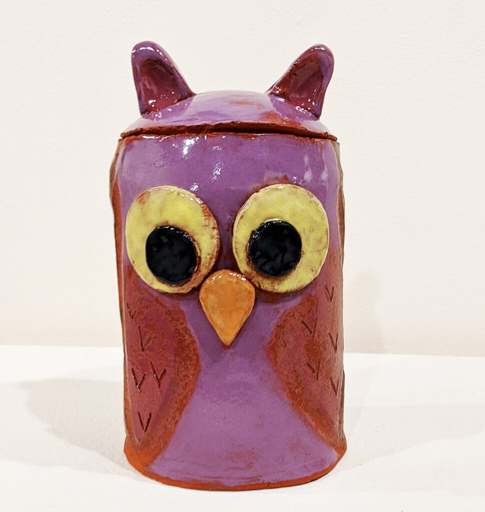 A purple ceramic cylinder decorated with eyes and beak like an owl
