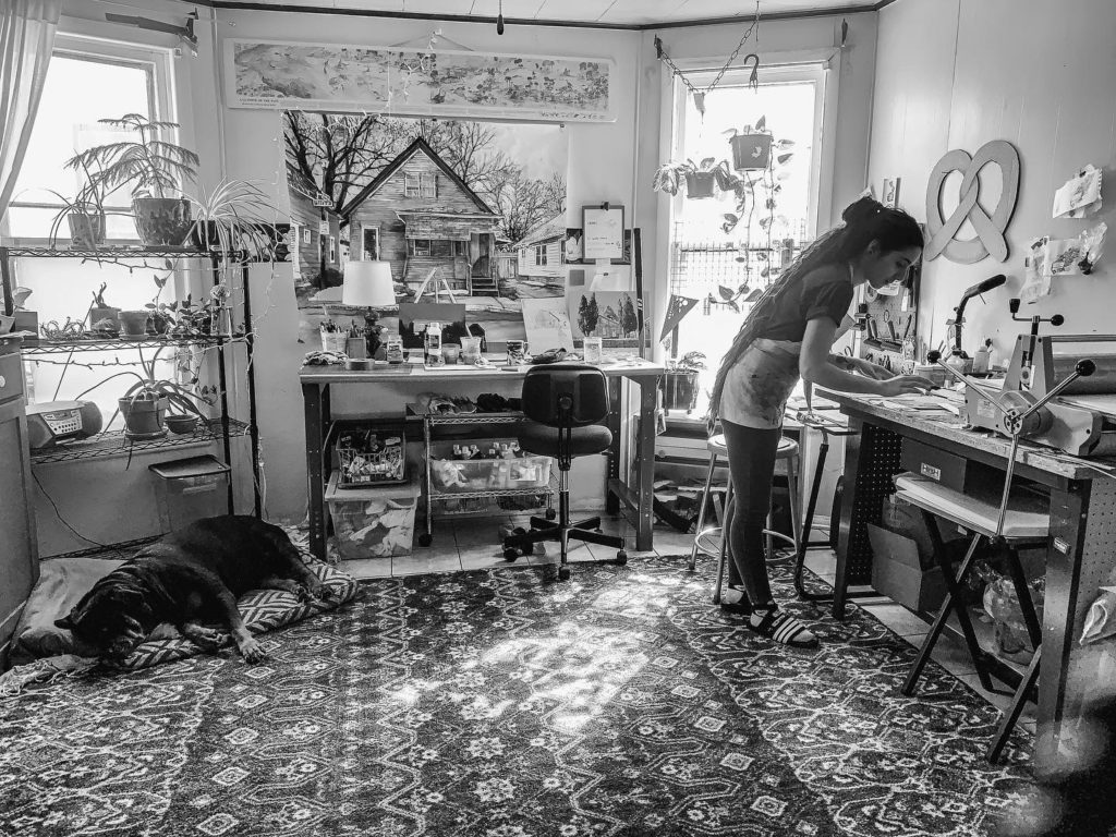 Black and white photo of Lizz deSimone bent over her desk in her busy studio