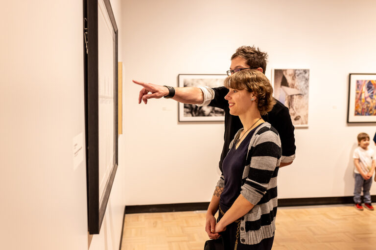Two museum visitors smiling and looking at artwork on the wall