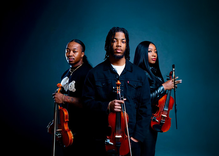 The three members of the Vibrant Strings trio against a dark blue background.