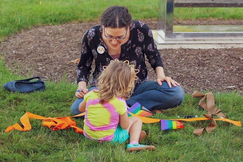 A parent and child writing a message on a ribbon to hang at Pride Celebration Day 2022.