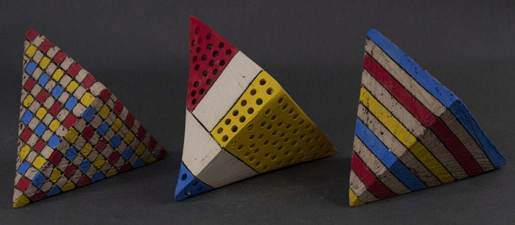 Three triangular prisms painted red, yellow, and blue in geometric patterns