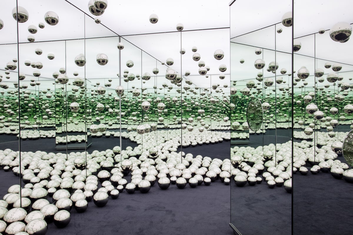 Interior of a mirrored room with a black floor and silver balls.