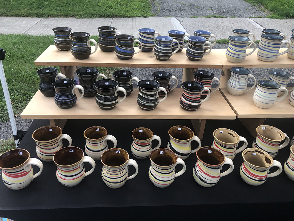 Three shelves filled with rows of ceramic mugs.