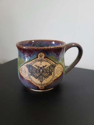 Ceramic mug with a astrology-themed moth design etched into the side.