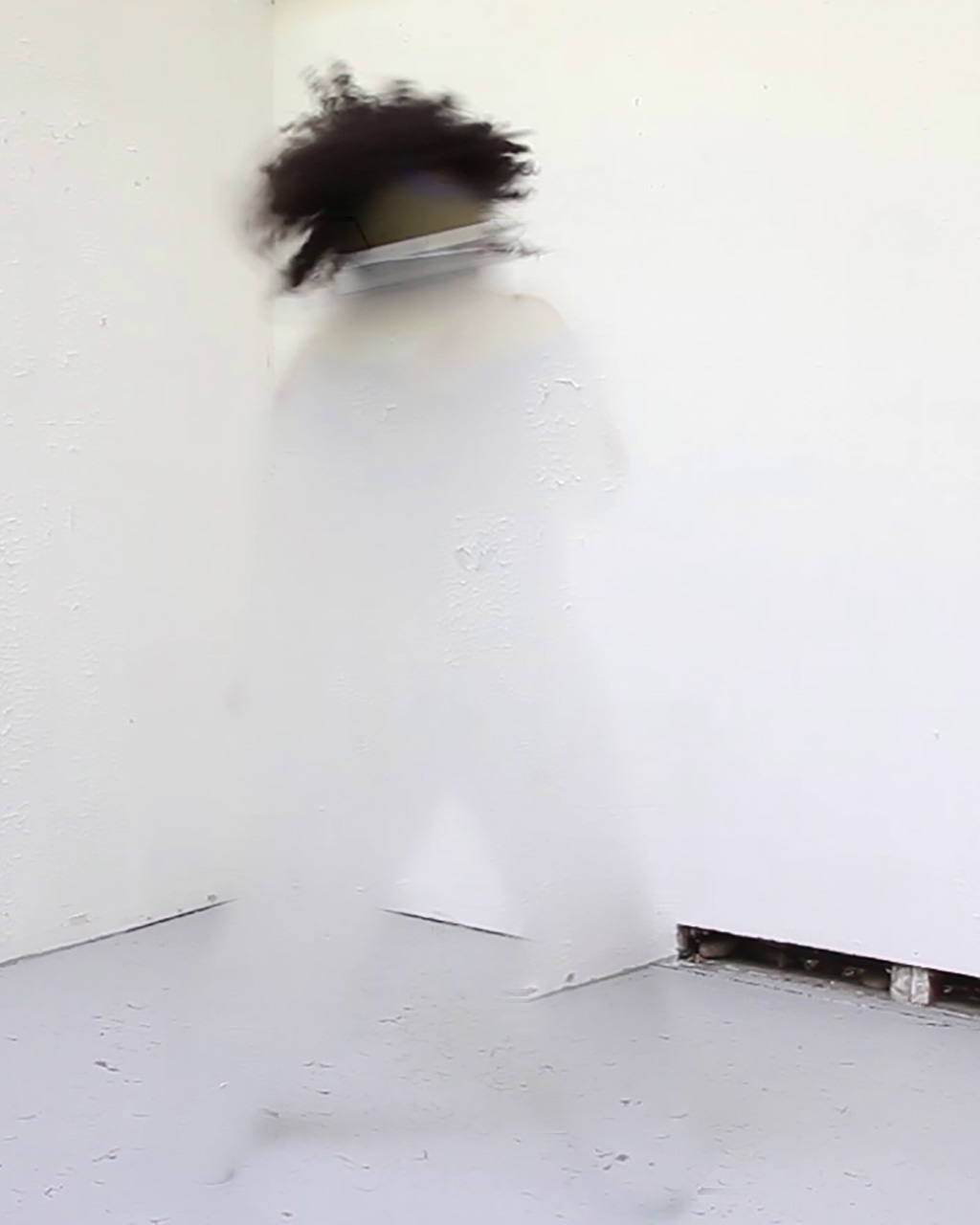 Still from a video of a black person dressed in white and moving against a white background, almost completely erased by digital blur.