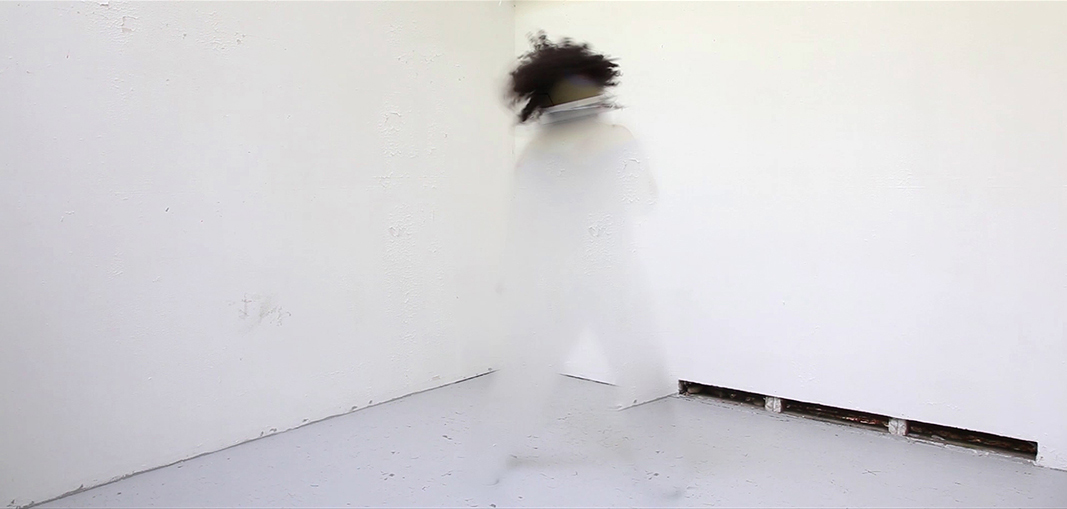 Still from a video of a black person dressed in white and moving against a white background, almost completely erased by digital blur.
