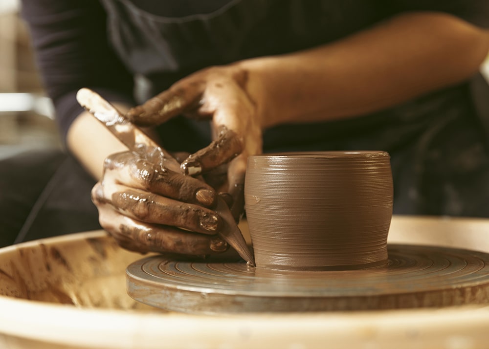 Hands using a clay tool to edge a clay pot on the wheel.