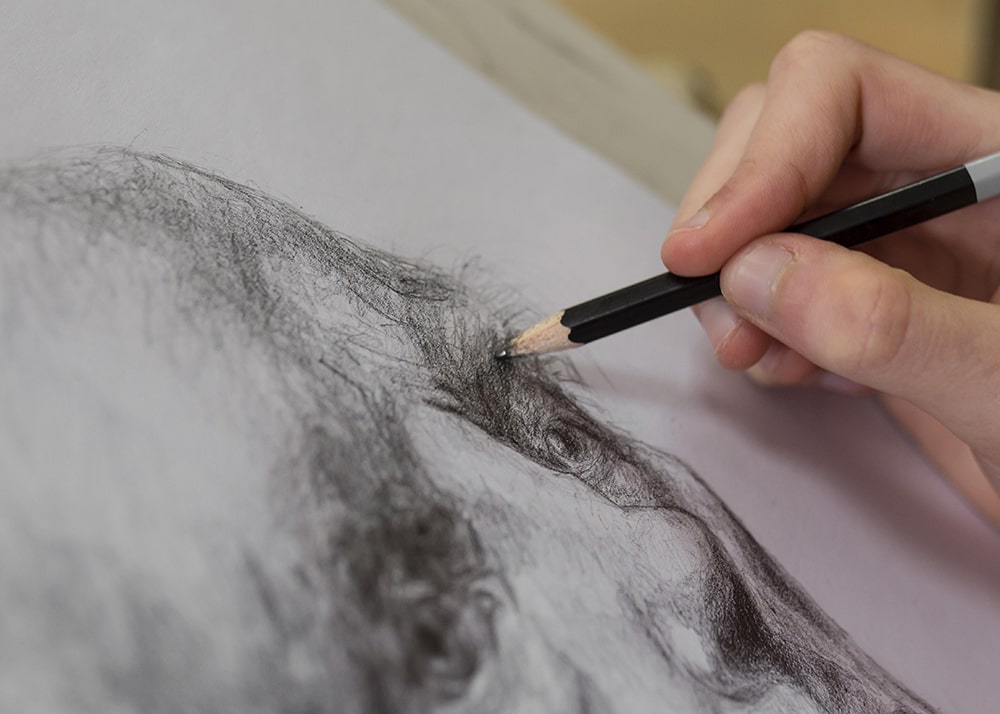 Hand with a pencil sketching a face.