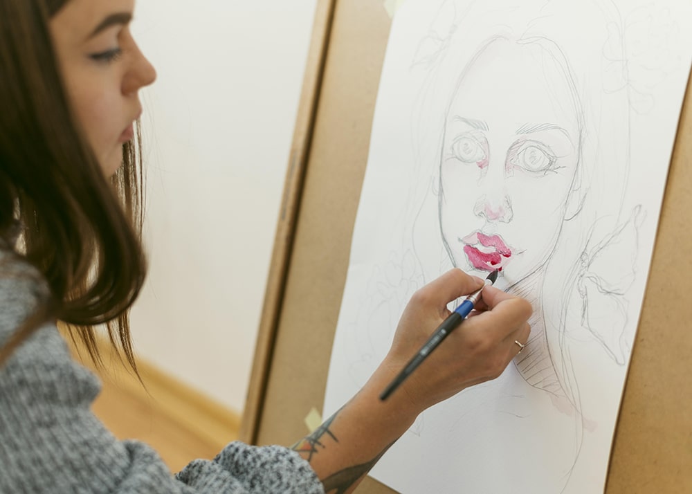 Young woman with brown hair painting an image of a face with pink lips.