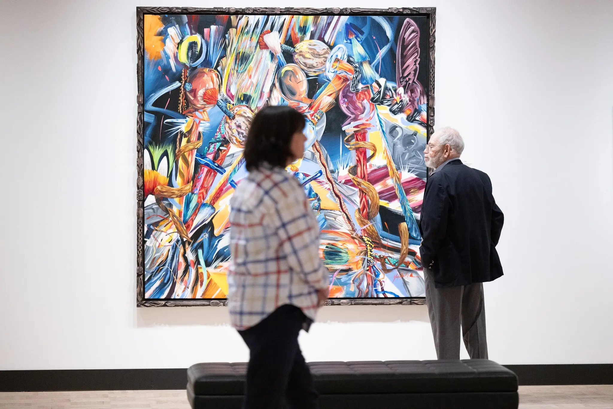 People walking in front of a bright, colorful painting on view in 'Past Forward: Native American Art from Gilcrease Museum.'