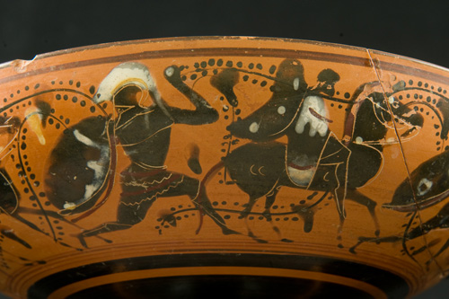 Painted black warriors in Greek armor do battle against a red background on the side of a ceramic bowl.